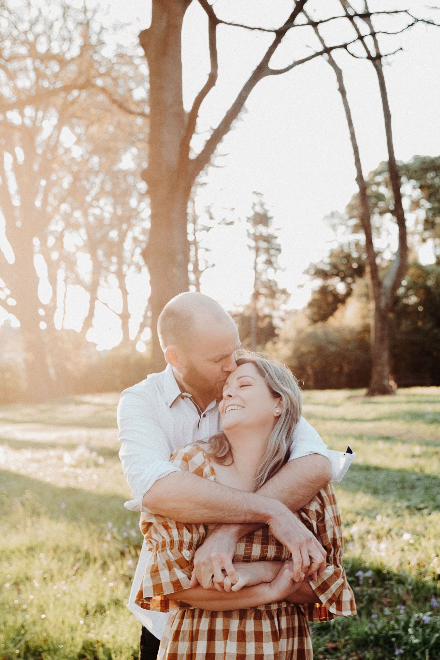 Romantic couple embracing in a sunlit forest during golden hour.