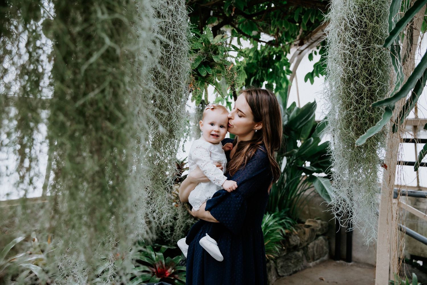 Mother and child sharing a moment surrounded by hanging plants in a greenhouse.