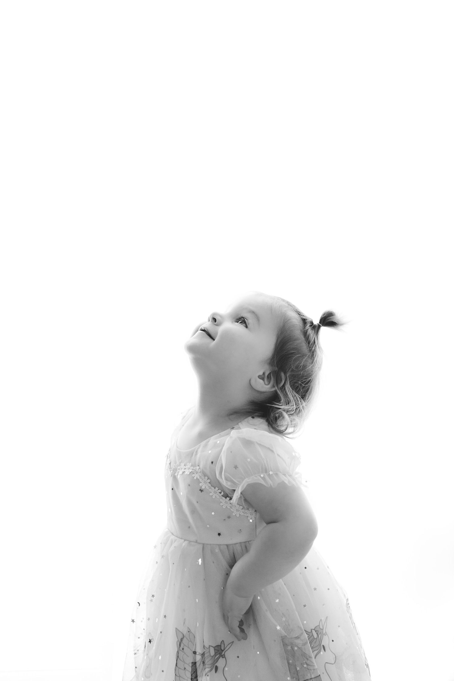 Black and white portrait of a young child in a lace dress looking up with wonder.