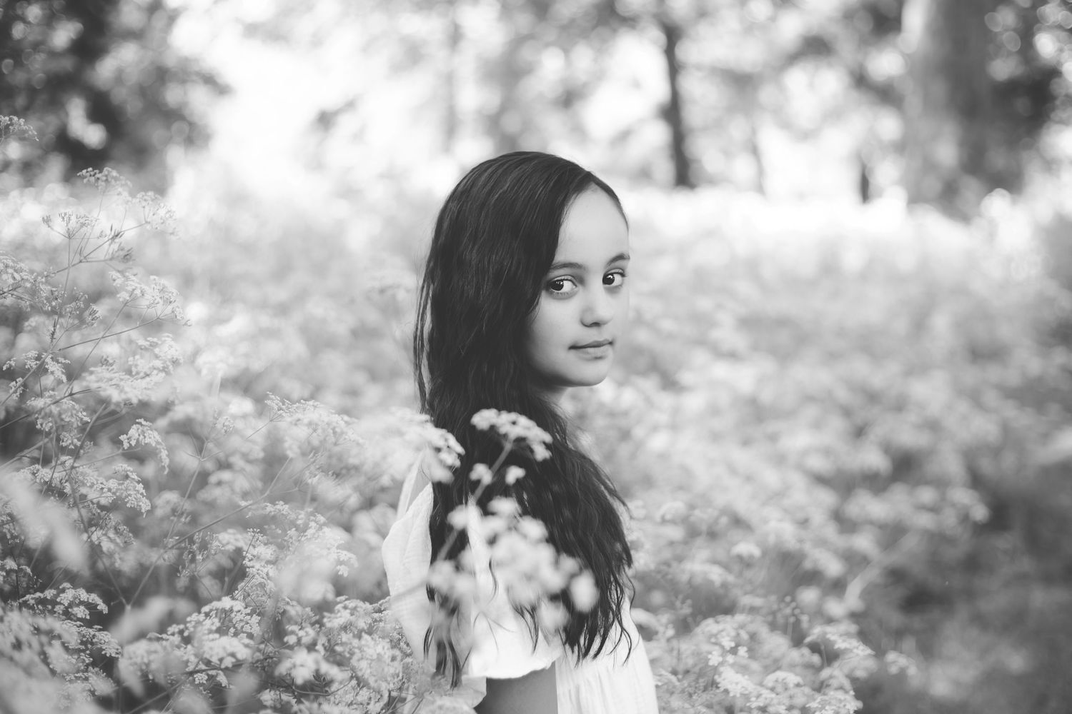 Black and white portrait of a girl looking over her shoulder in a field of flowers.