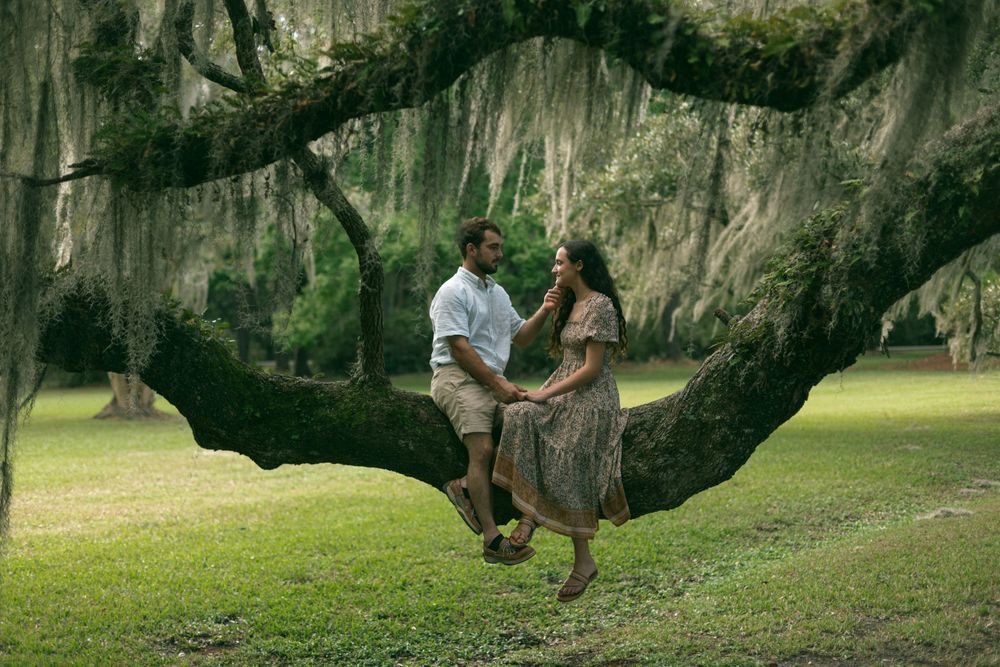 A romantic moment shared on a moss-draped tree branch in a lush Southern garden.
