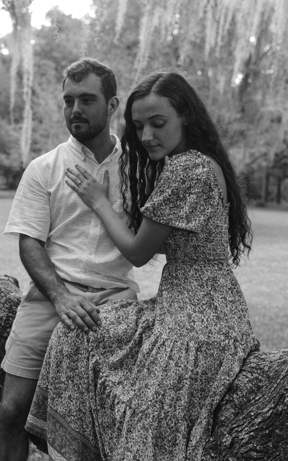 A black and white portrait of a couple sharing an intimate moment on a tree branch.