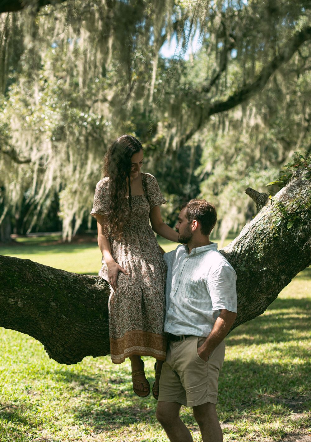 A romantic scene unfolds beneath Spanish moss as a couple explores a curved tree branch.