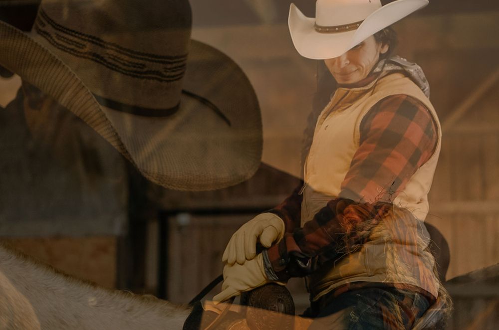 Western style cowboy rider in tan vest against moody sepia background.