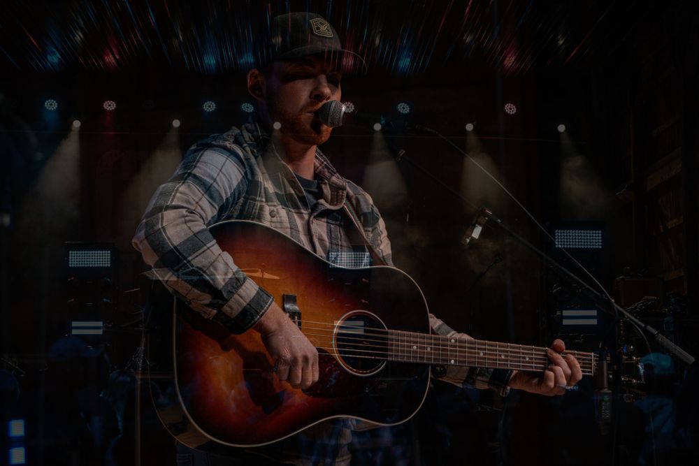 Musician performing with acoustic guitar on dimly lit stage with blue lighting effects.