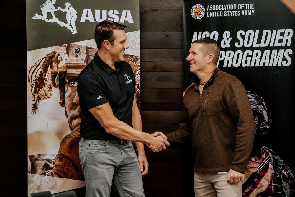 Two people shake hands while standing in front of an AUSA banner and NCR and Soldier Programs signage.