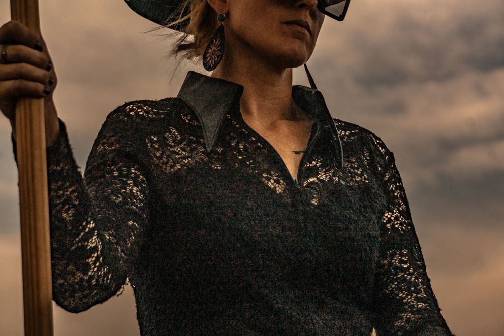 Dramatic sunset portrait of person wearing black lace top and sunglasses.