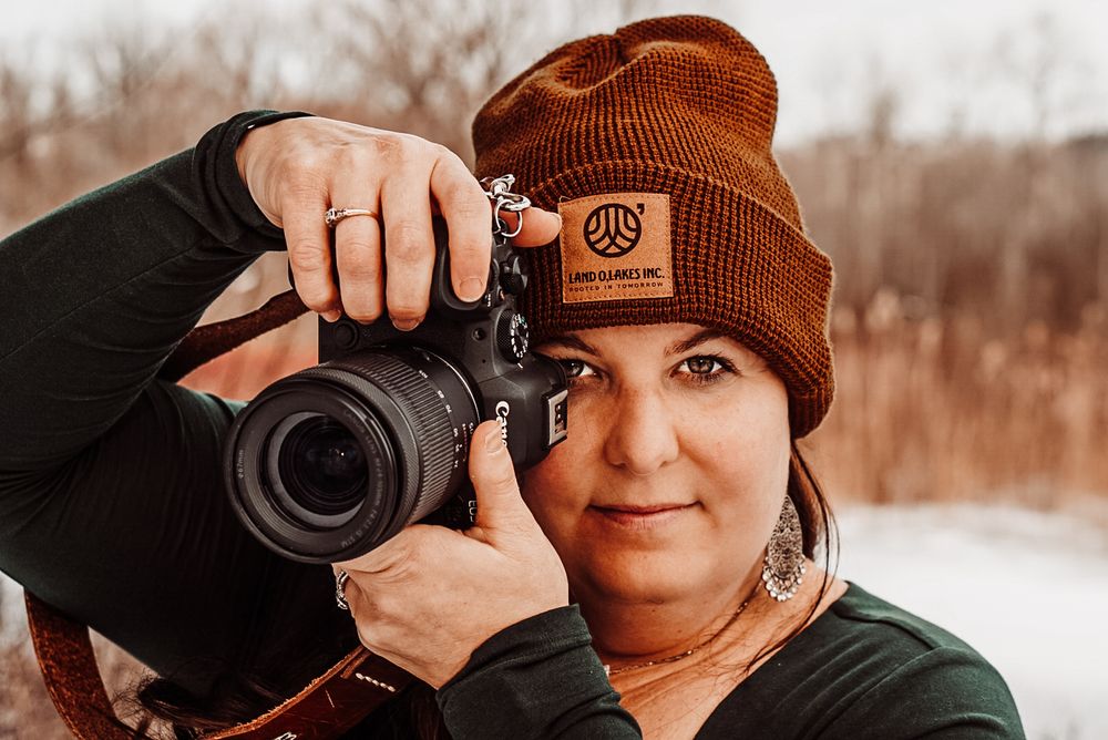 A photographer wearing a brown beanie and holding a professional camera in winter setting.