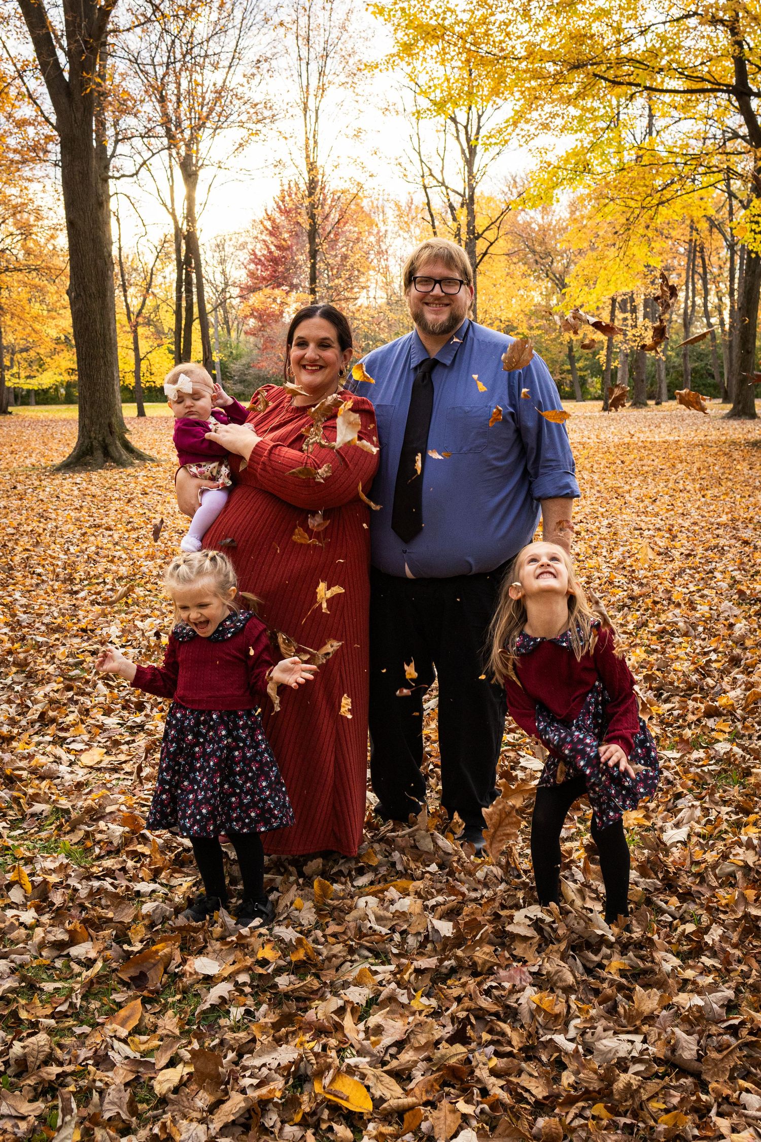 Family group photo with children playing in fallen autumn leaves.