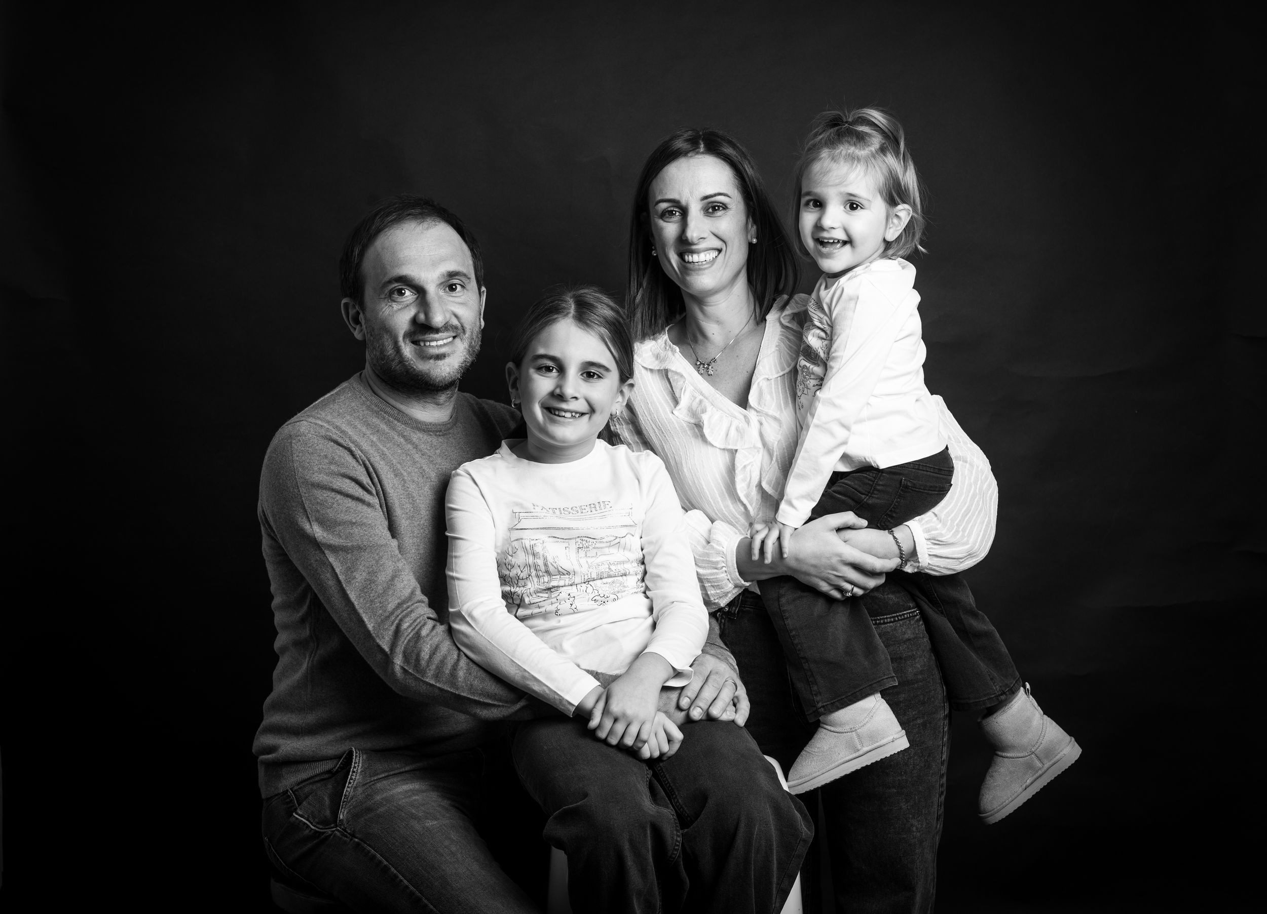 Black and white portraits showing a family posing together in matching dark outfits against a dark background.