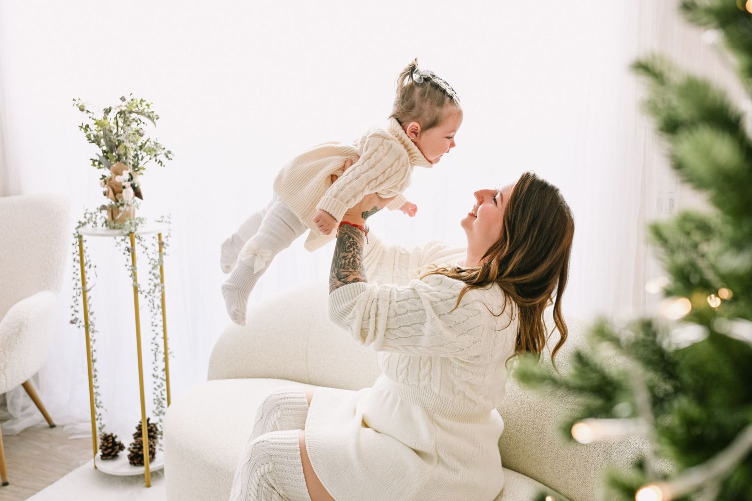 Light and airy family portraits with white sweaters and holiday decorations in the background.