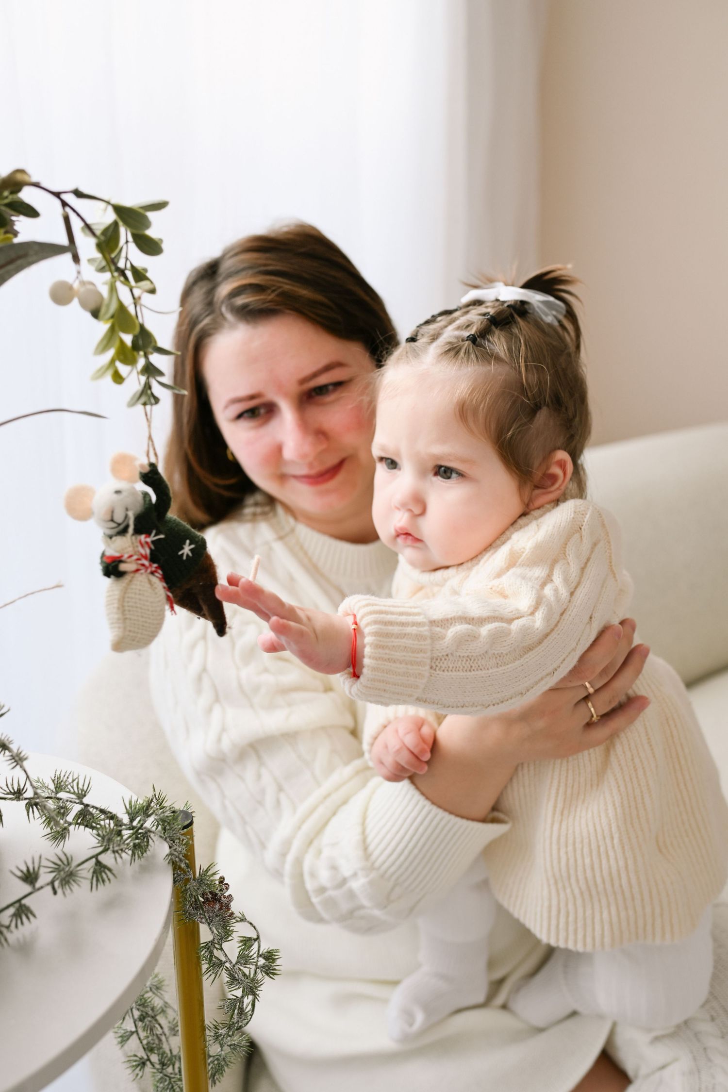 Sweet moments between parent and child in matching cream sweaters near decorative branches.