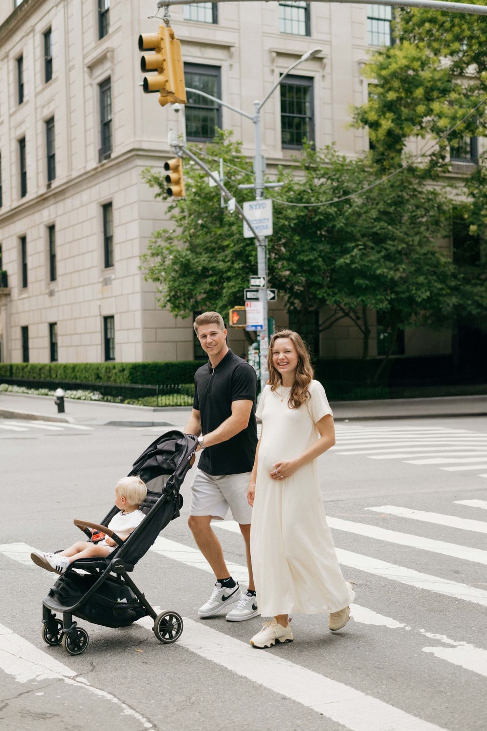 A couple playfully poses with their stroller on a city street corner near stone buildings.