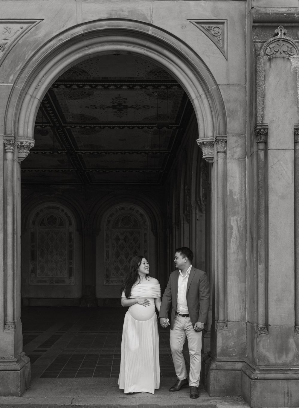 A sequence of black and white photos showing a couple walking and posing under ornate stone archways in a courtyard.