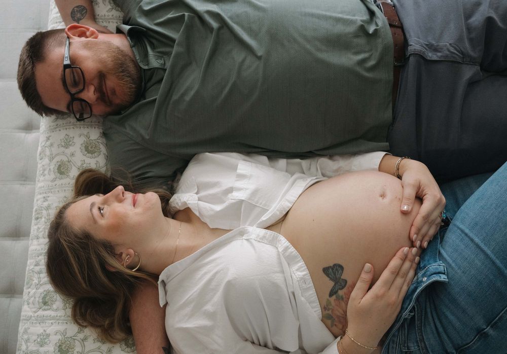Couple laying on carpet together during intimate maternity photoshoot with visible baby bump.