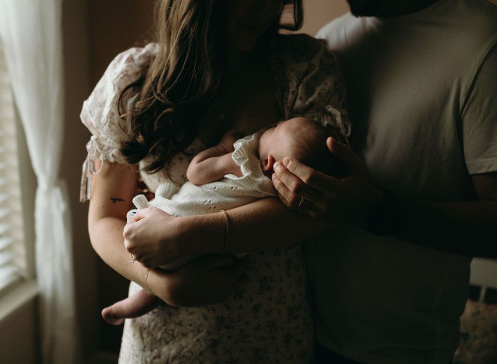 A series of intimate maternity photos showing a pregnant woman in a white lace dress by a window in moody lighting.