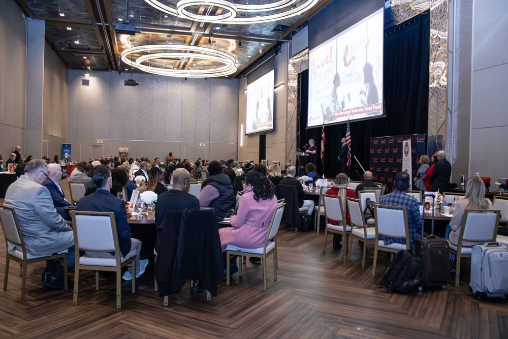 A panoramic view of a modern conference room with circular chandeliers and people seated at round tables during an event.