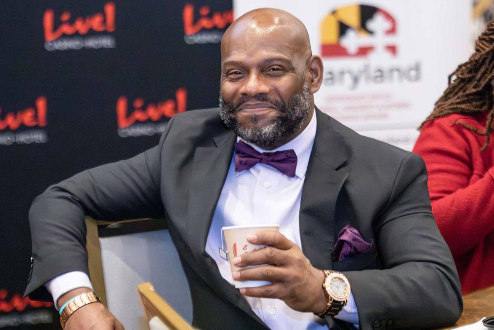 A person in a black suit and purple bow tie smiles while looking at a mobile phone at an event.