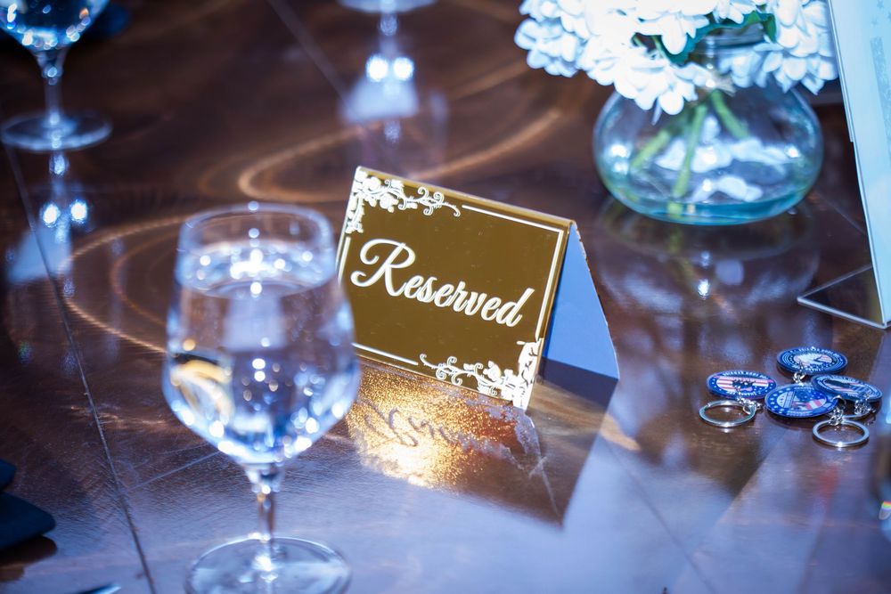 Elegant reserved table sign with floral details glows on a table set with wine glasses and blue floral centerpieces.