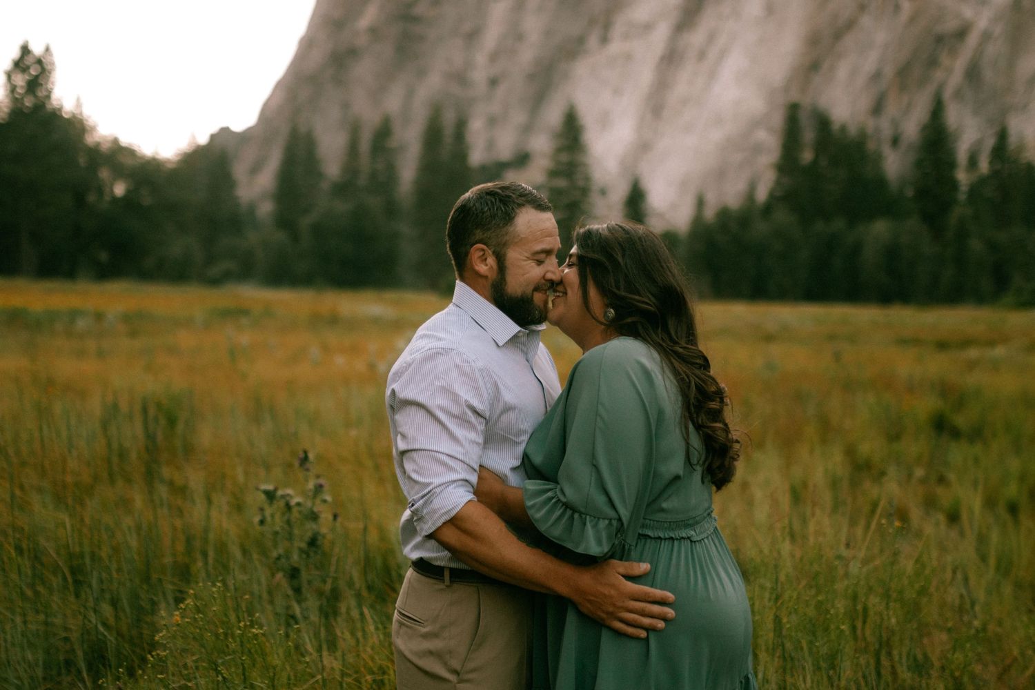 A romantic couple embraces against the majestic backdrop of Yosemite Valley's granite cliffs and mountains.