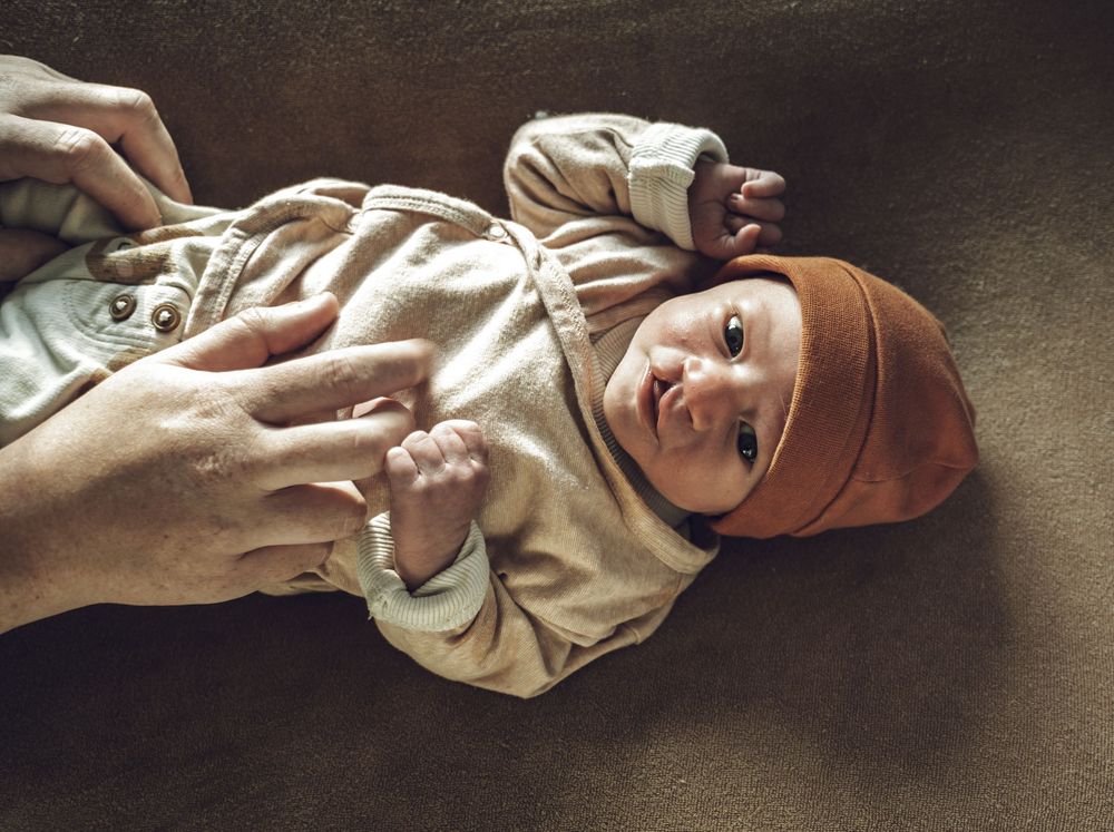 A sequence of seven images showing a baby lying on their back in a beige onesie on a dark surface.