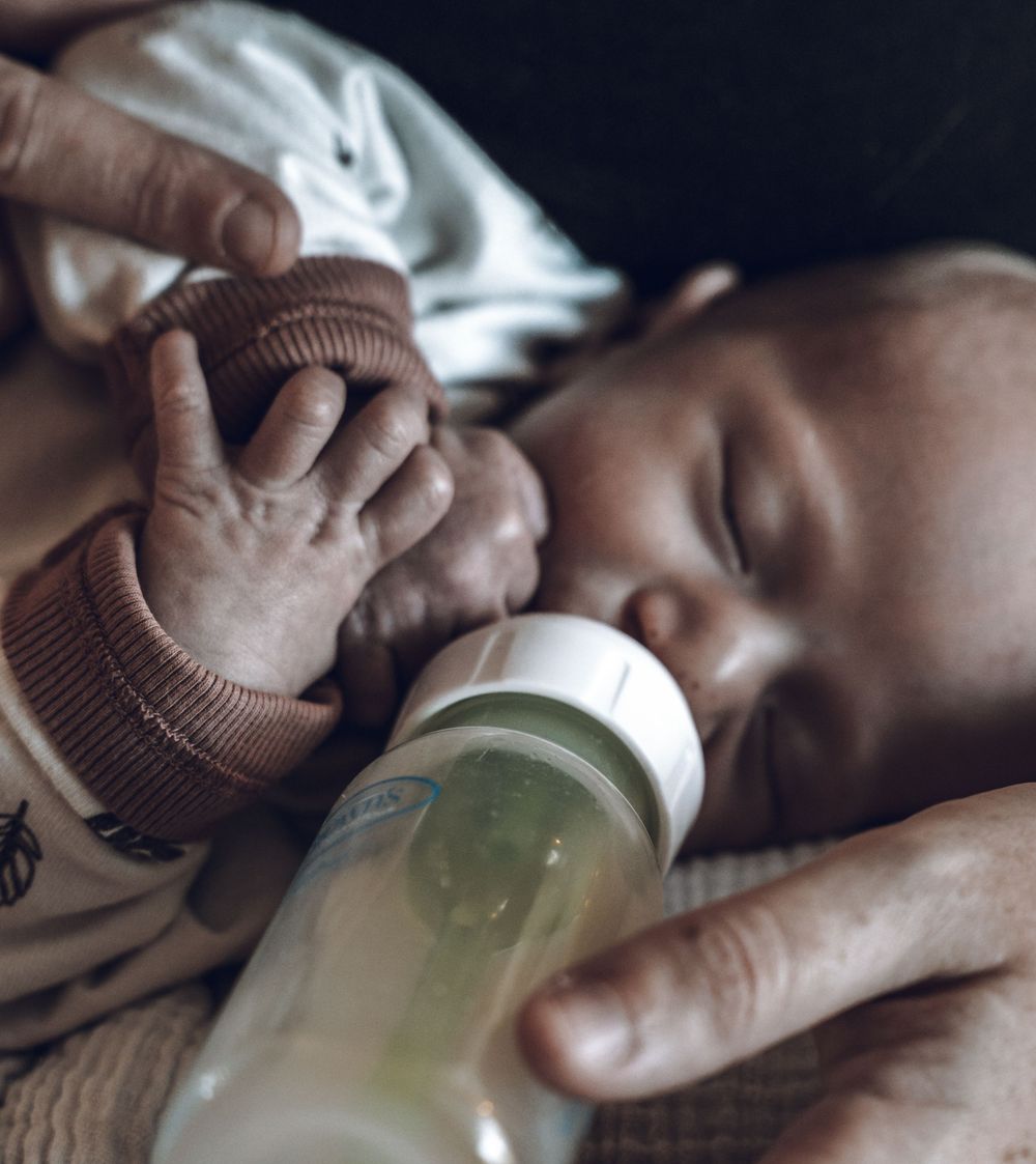 A baby bottle being filled with milk or formula while being held in someone's hands.