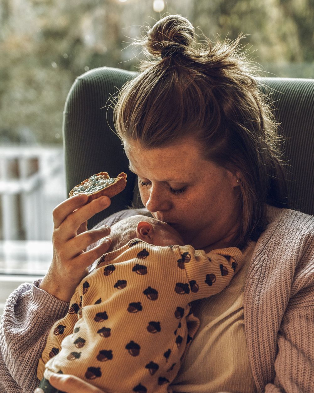 Person in a brown sweater snuggling with a baby wrapped in a polka dot blanket in natural lighting.