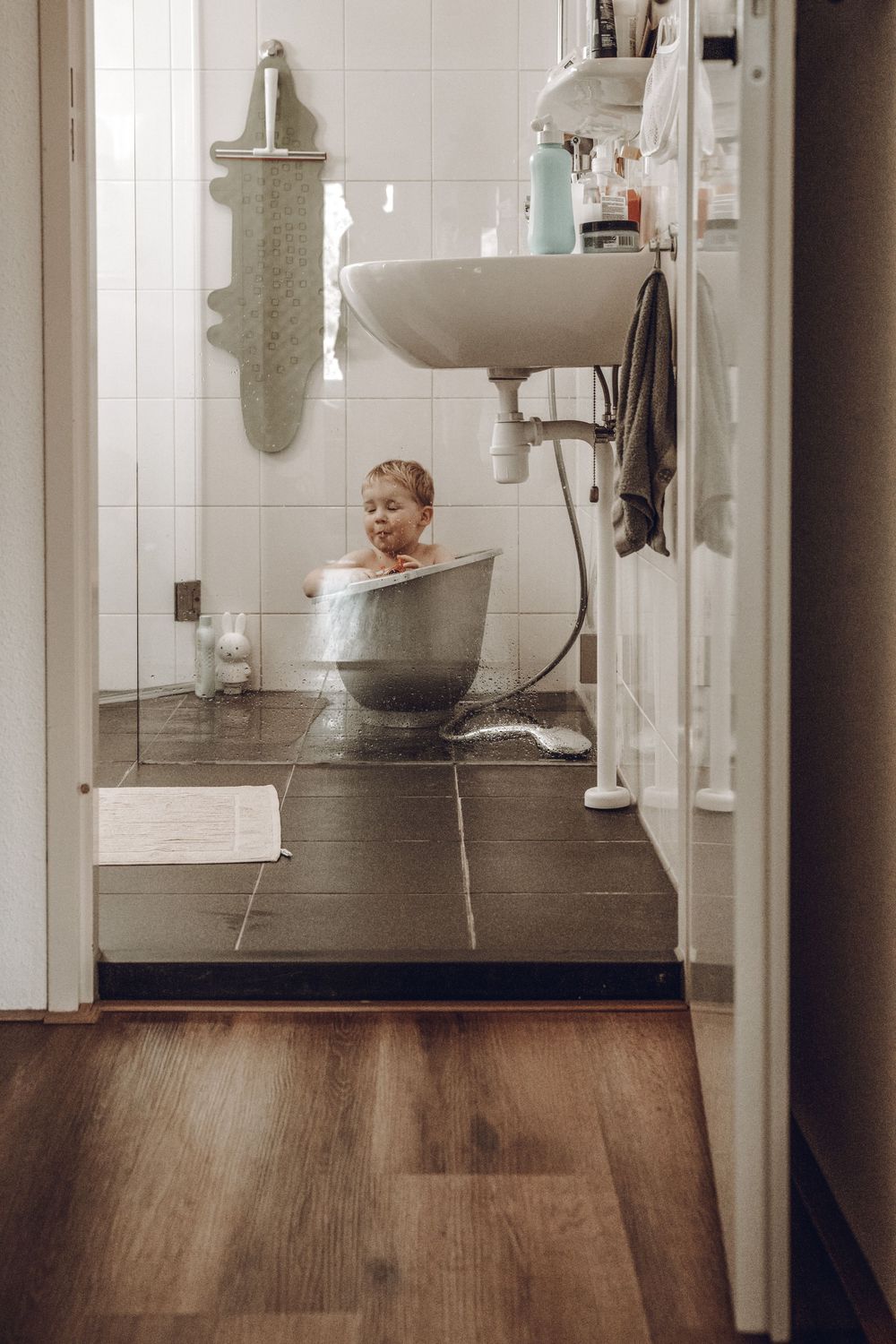 White bathroom interior with dark wood flooring and modern fixtures captured in mirror reflections.