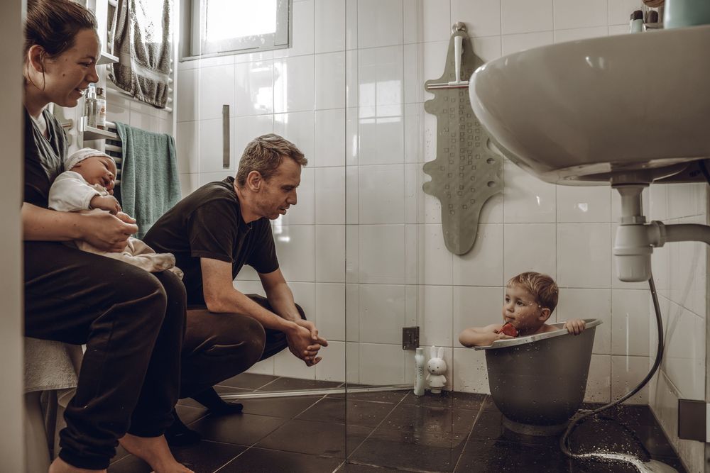 Parent and child brush teeth together at bathroom sink while looking in mirror.
