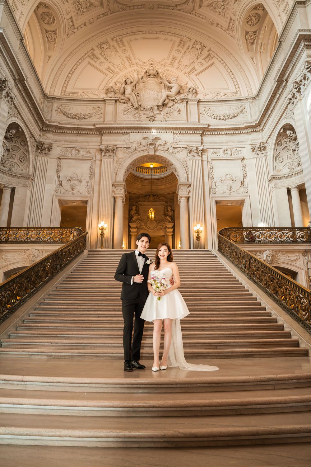 A couple poses on an ornate marble staircase inside San Francisco City Hall's grand Beaux-Arts interior.