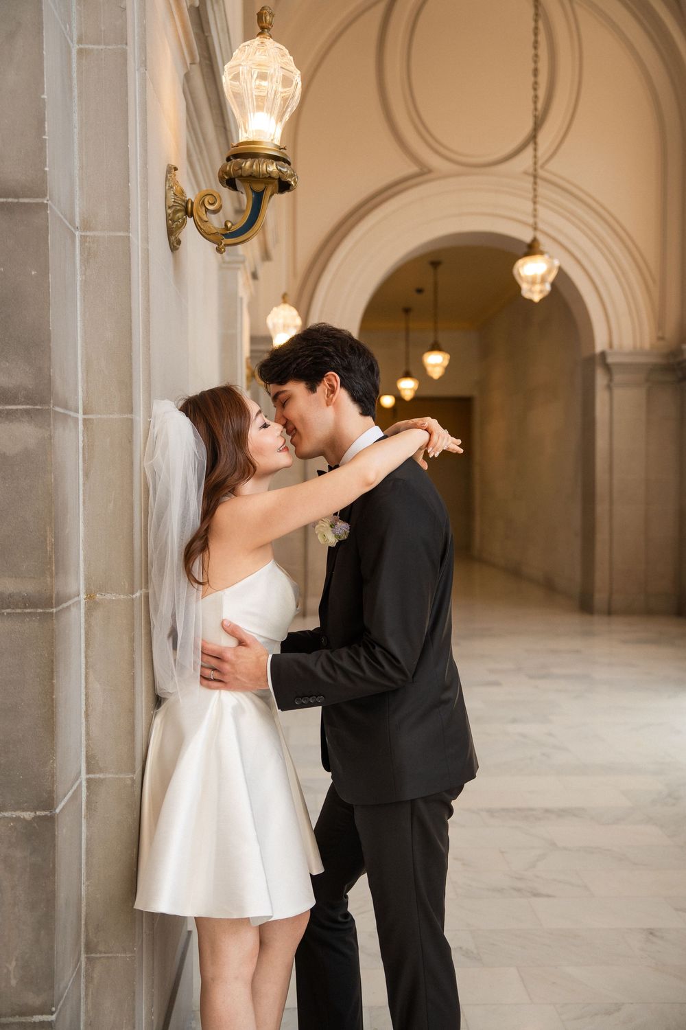 Couple shares intimate dance moments in elegant white-columned hallway with arched ceilings.
