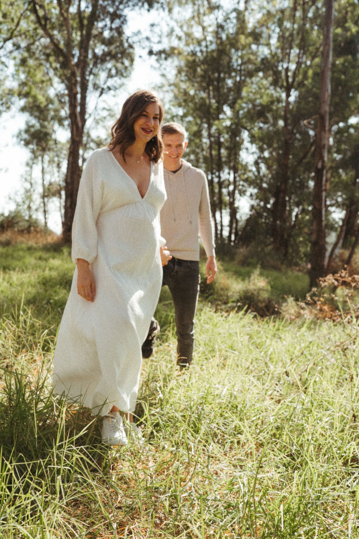 Romantic couple in white clothing walking through tall grass in eucalyptus grove.