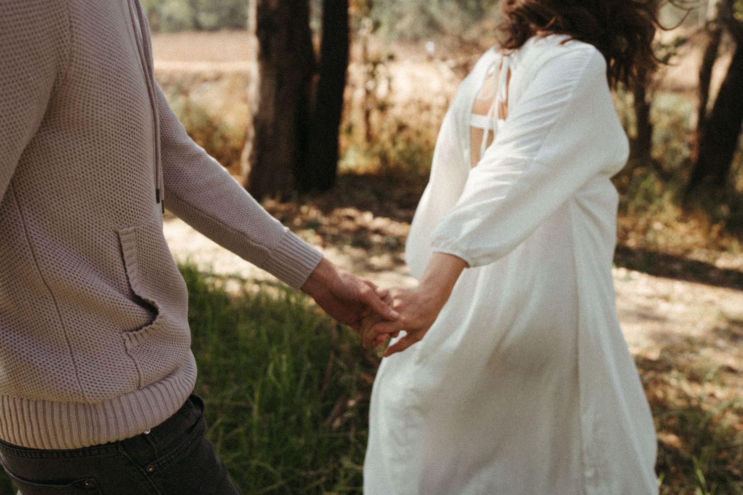 A romantic outdoor photoshoot in a sunlit field with a couple in white and beige attire.