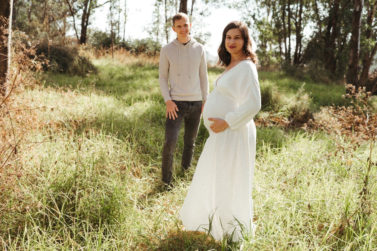 A couple shares intimate moments in a grassy field surrounded by eucalyptus trees.