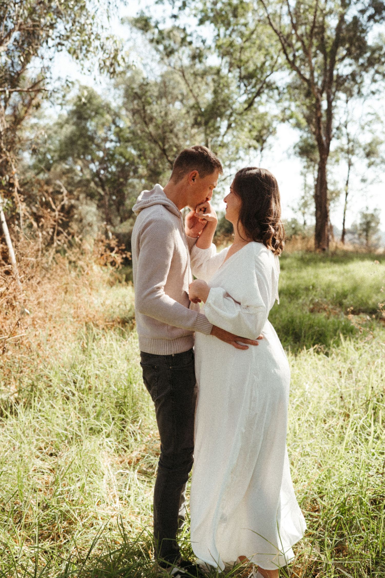 Couple sharing romantic moments in a sun-drenched field with eucalyptus trees.
