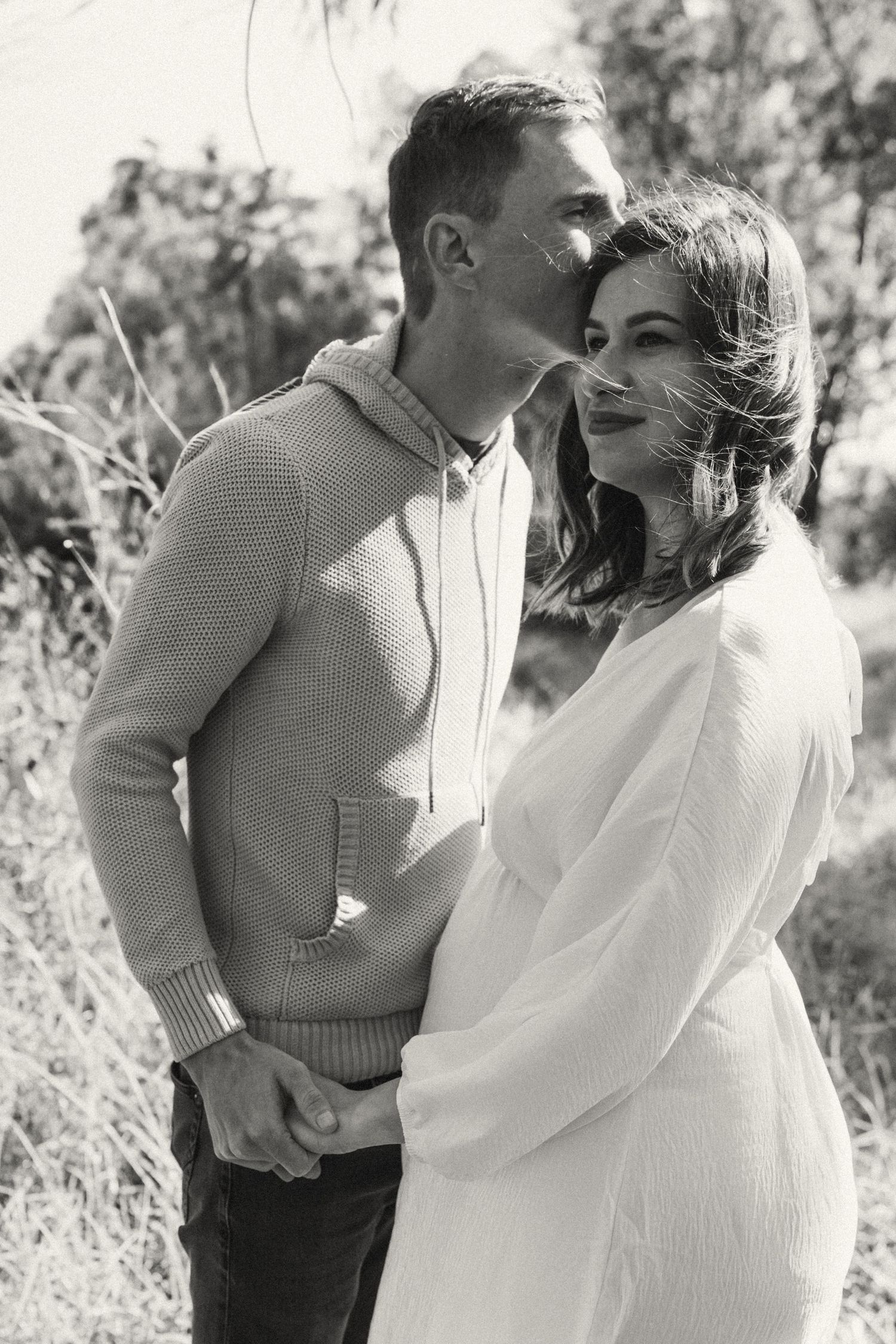 A romantic outdoor photoshoot featuring a couple in black and white, with a sweater and white dress in nature.