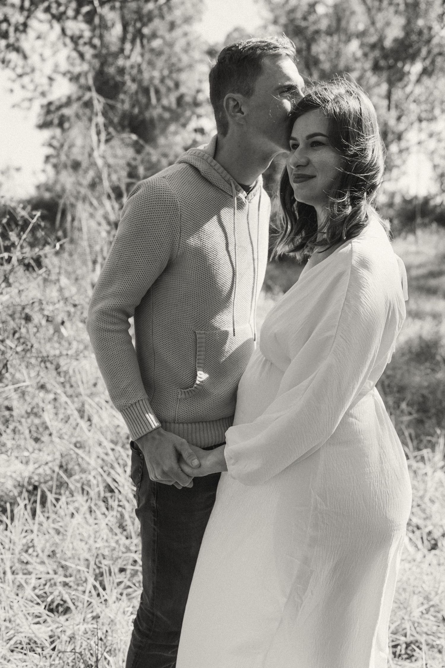 A tender moment captured between a couple in casual attire against a natural outdoor backdrop.