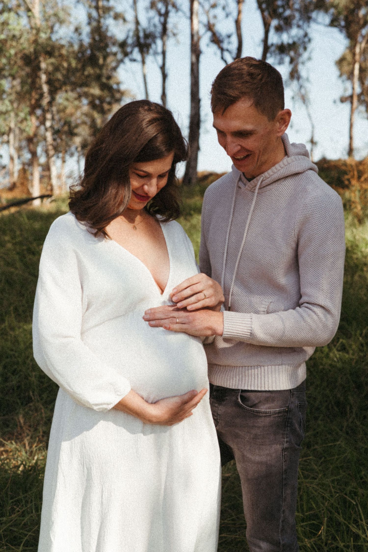 A loving couple shares tender moments in a grassy field during a sunny outdoor photoshoot.