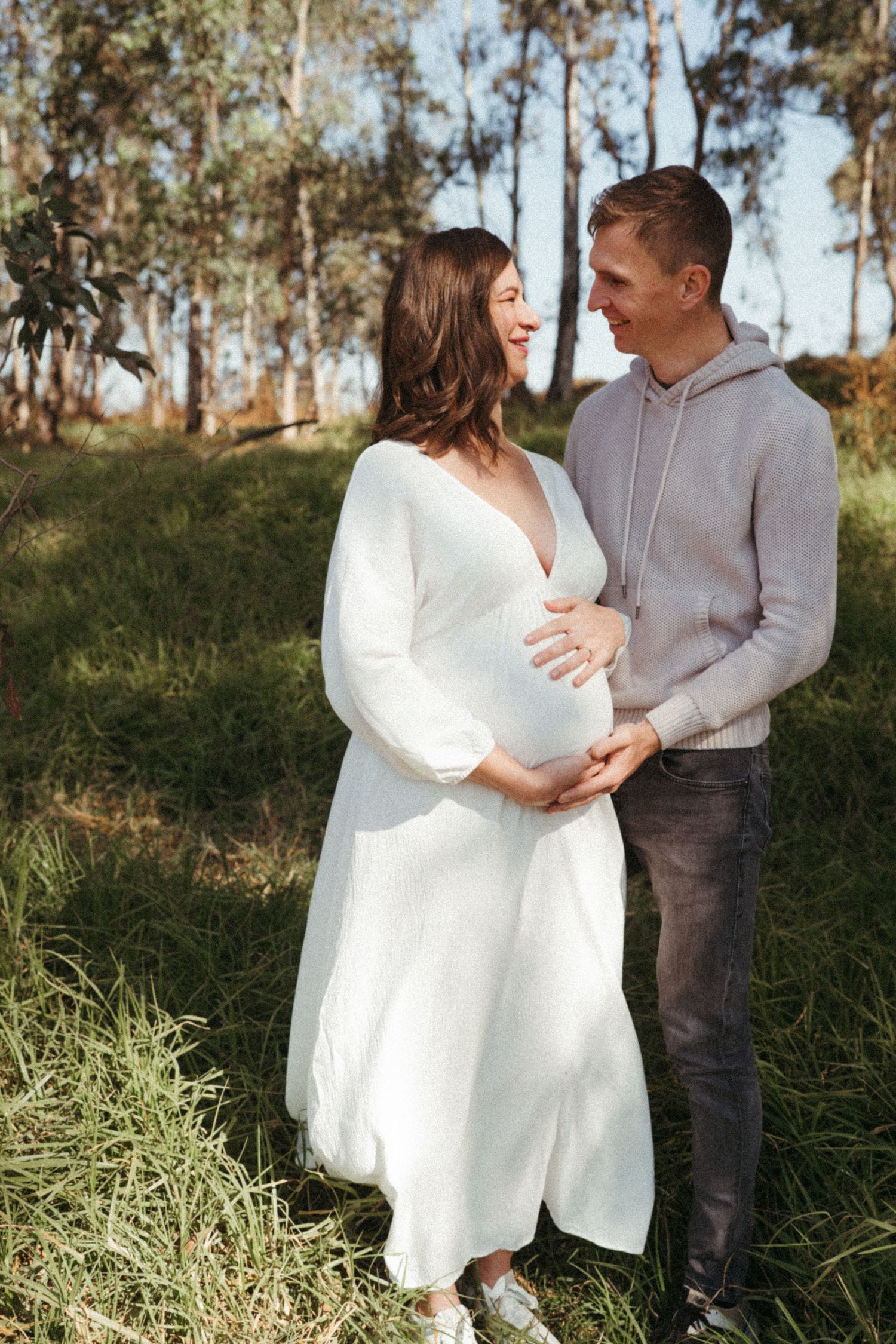 A couple embraces in a sunlit field wearing coordinated casual outfits.