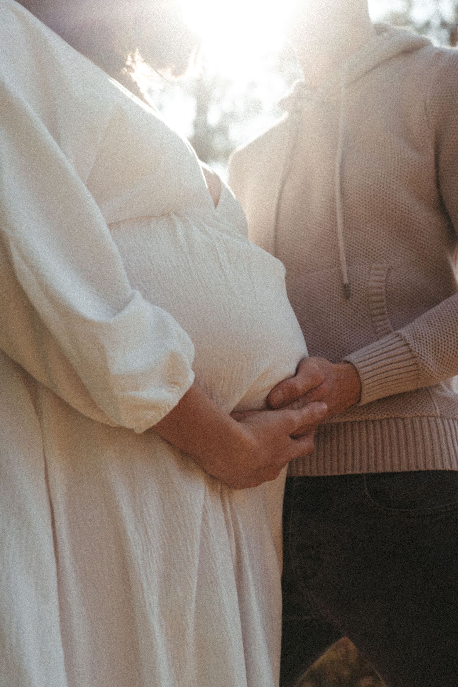 A couple in white and beige clothing embraces tenderly in an intimate outdoor photoshoot.