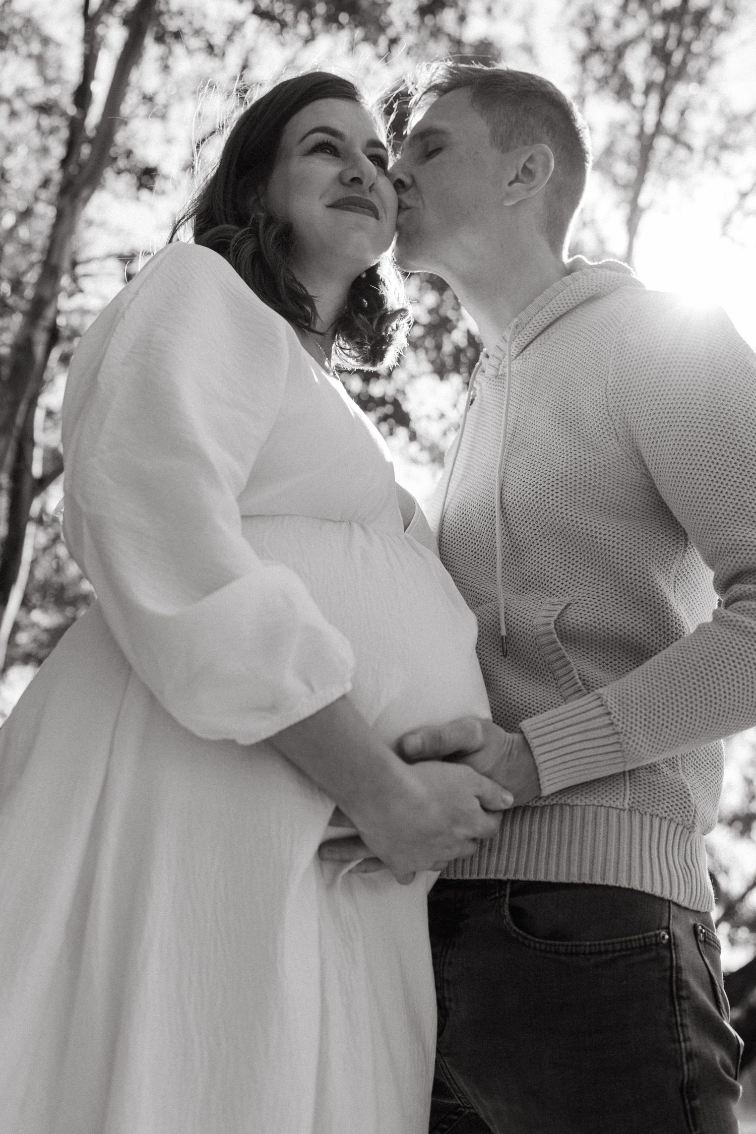 An intimate black and white portrait of a couple sharing a tender moment outdoors.