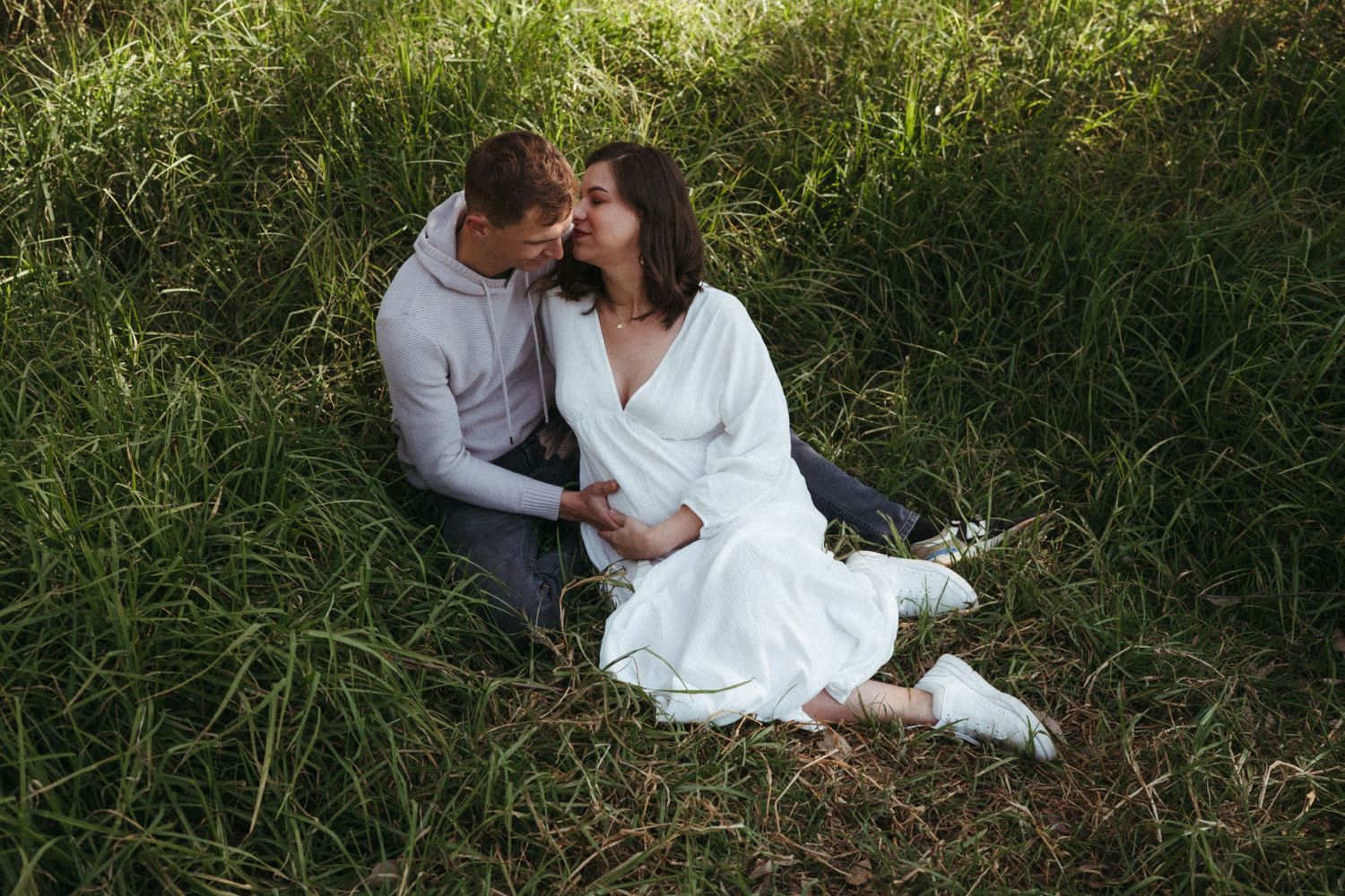 A romantic couple lounges in tall grass during a sunny outdoor photoshoot.