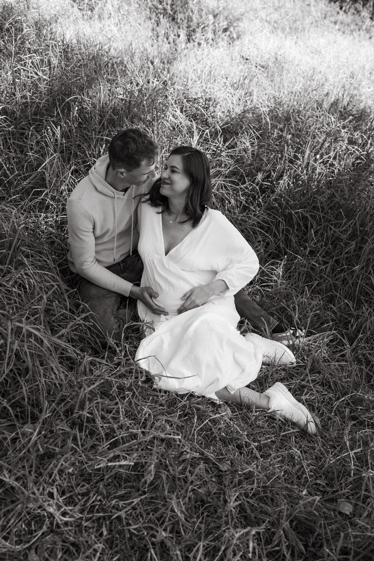A black and white photo captures a romantic moment between two people in tall grass.