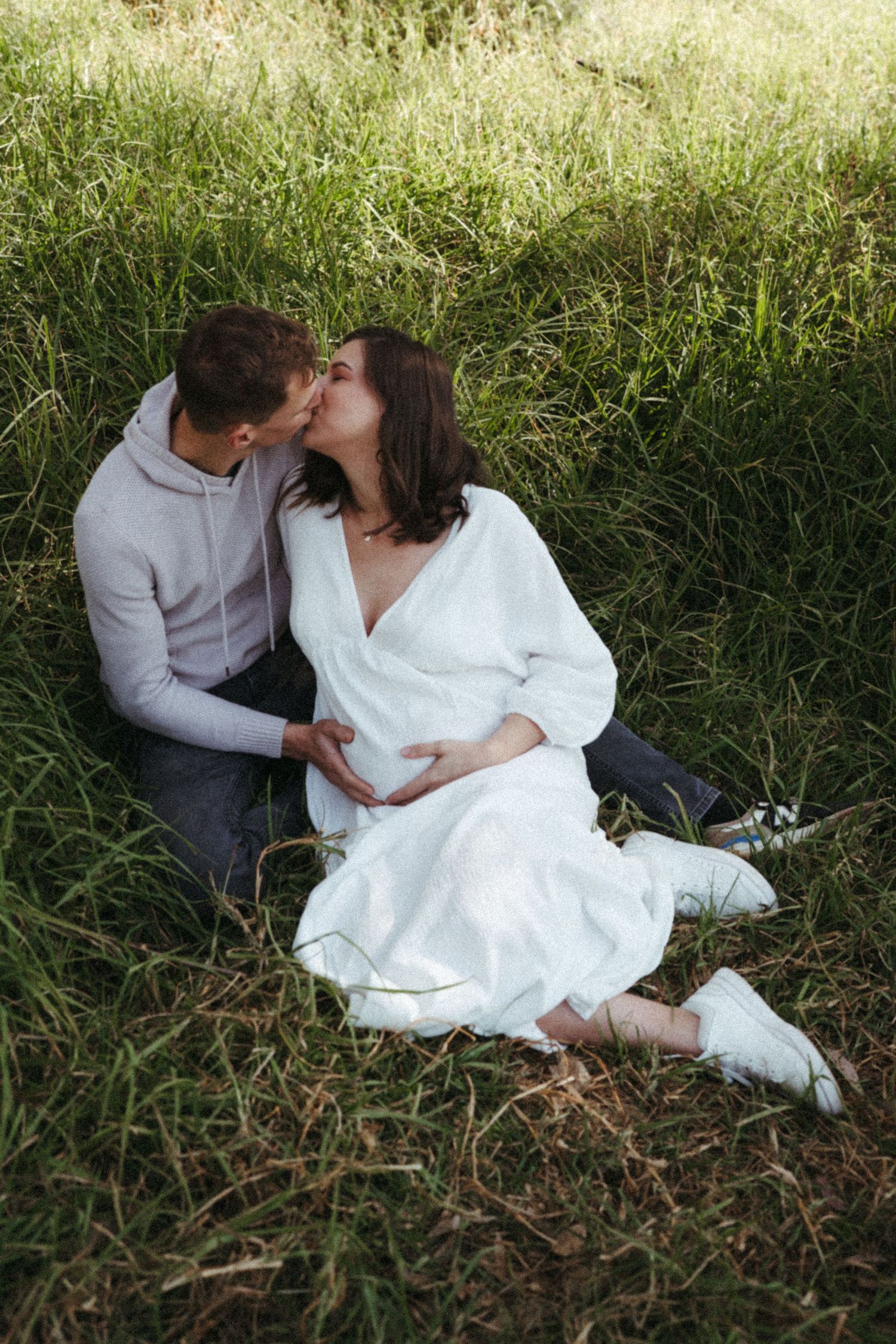 Two people share intimate moments while sitting together in sunlit grass.