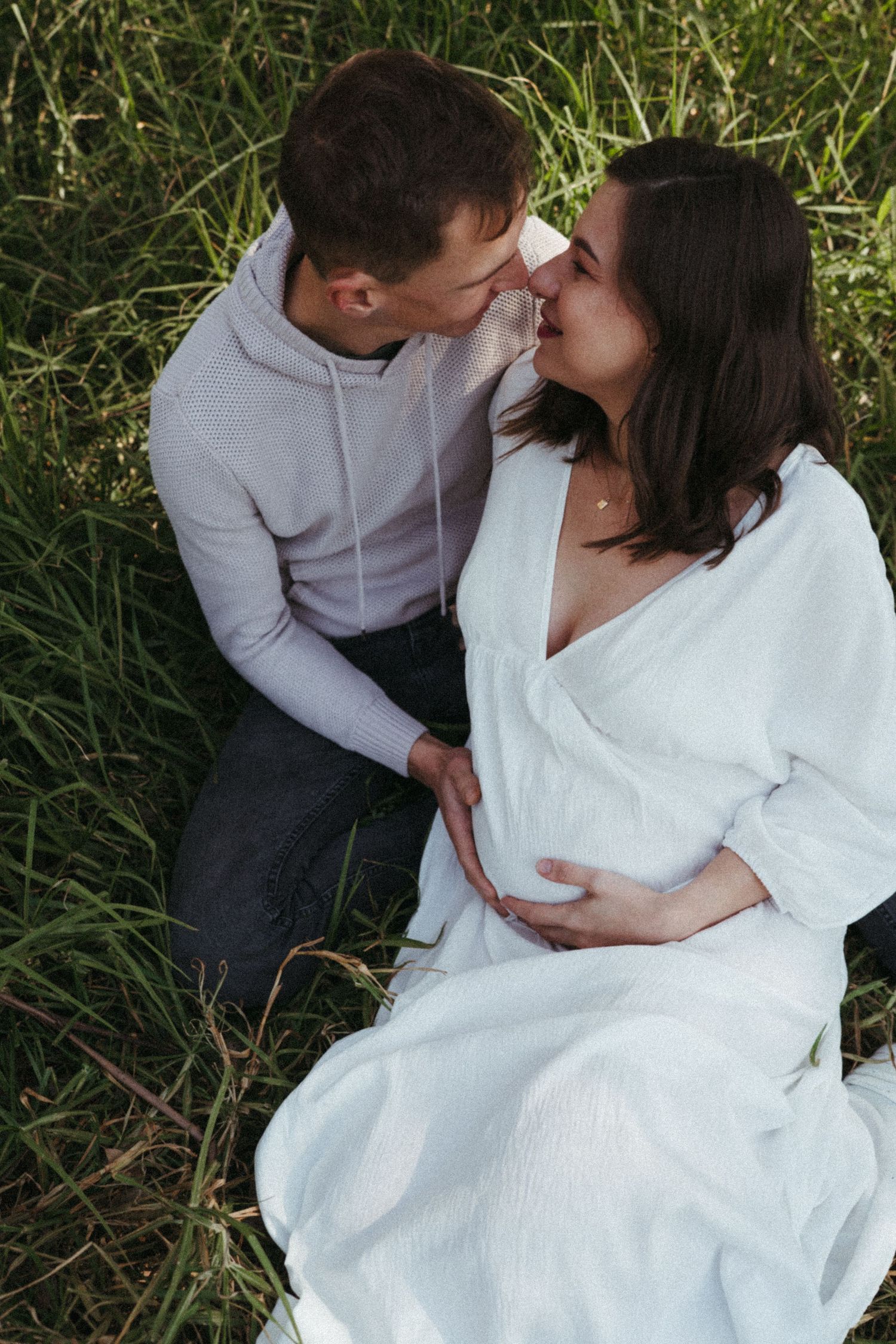 A couple in white and grey clothing shares tender moments during an outdoor photoshoot.