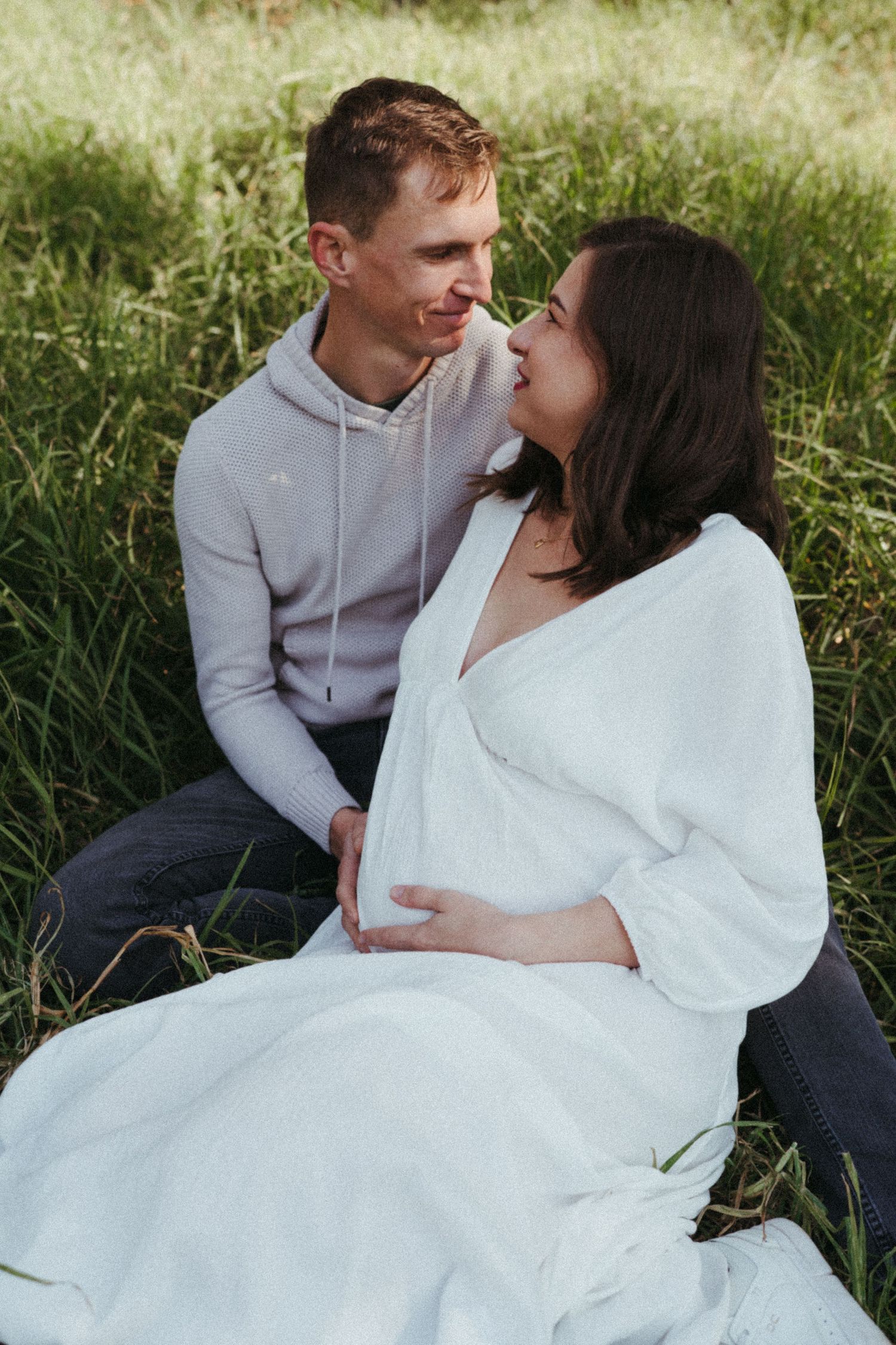 A couple in light colored clothing shares intimate moments in a sunlit field.