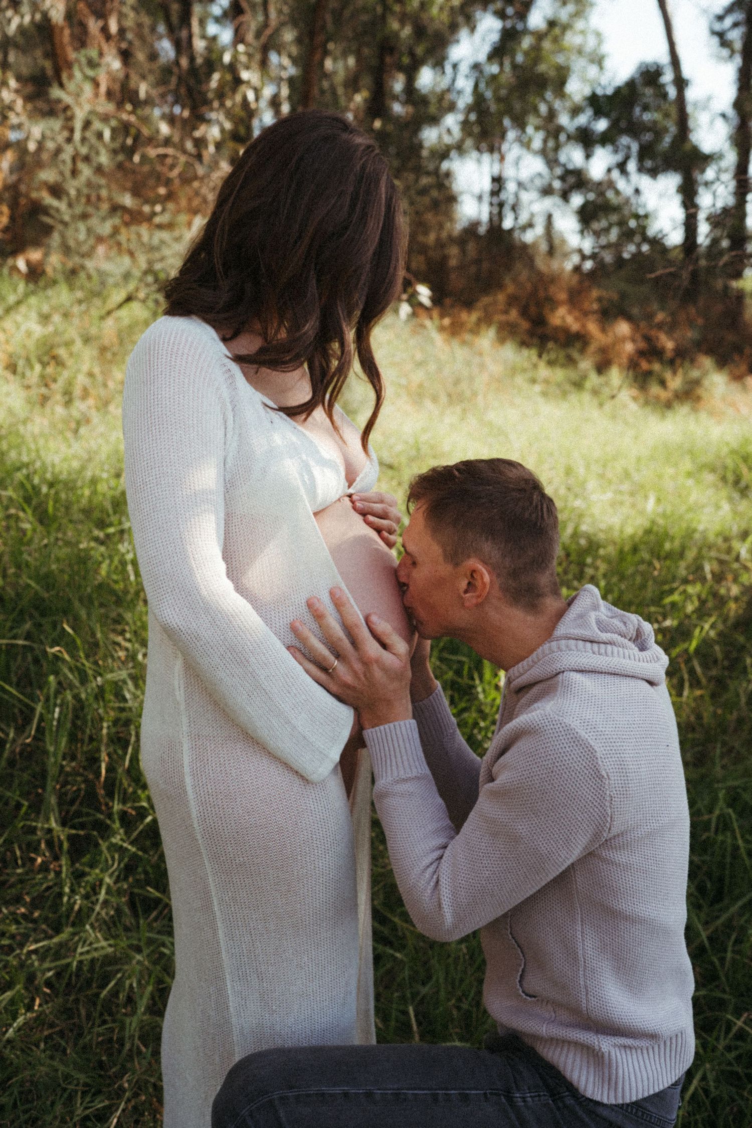 Tender pregnancy photoshoot with couple sharing intimate moments outdoors.