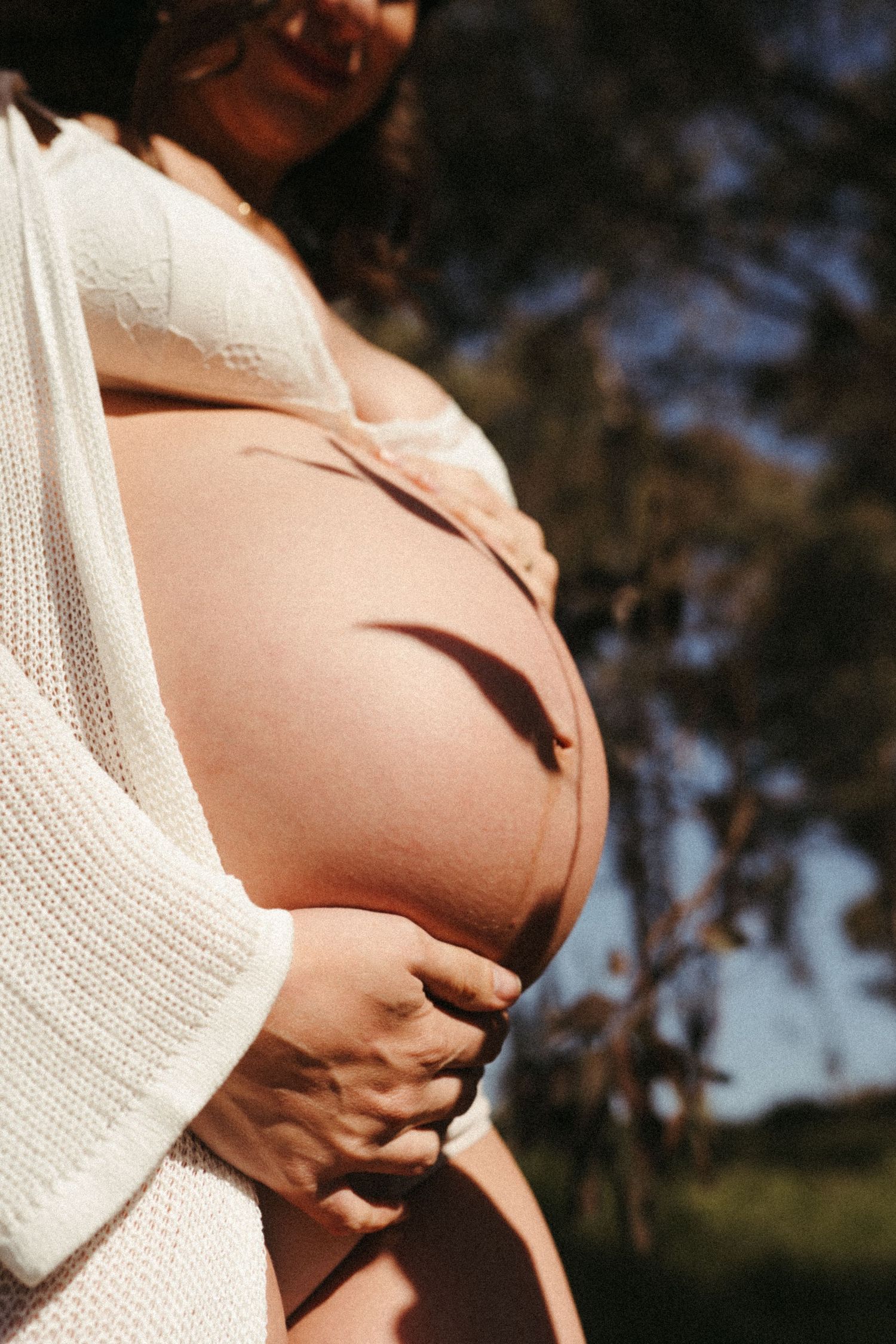 Warm-toned maternity portrait showing pregnant belly in soft sunlight.