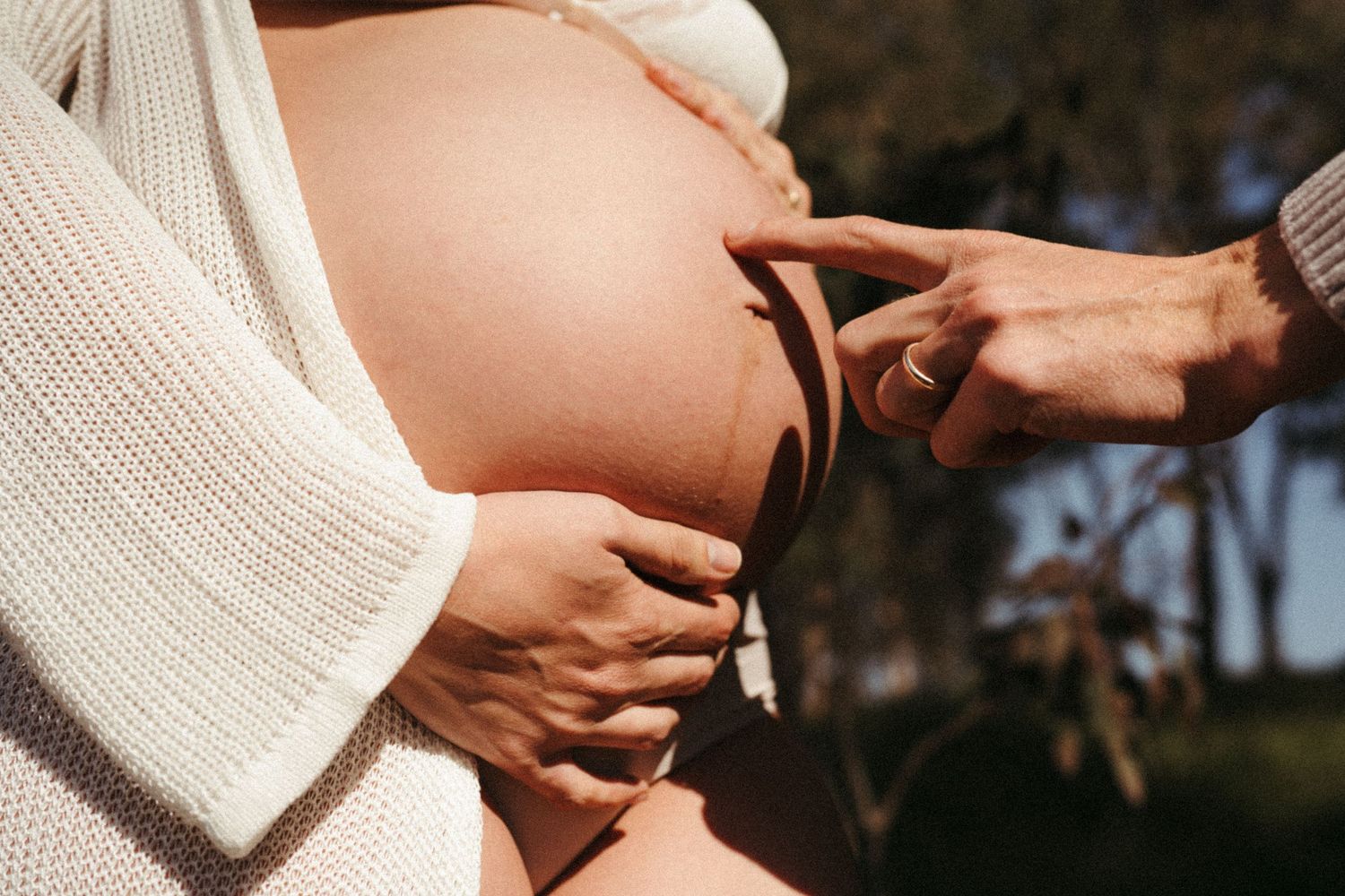 Close-up maternity photo with hands cradling baby bump outdoors.