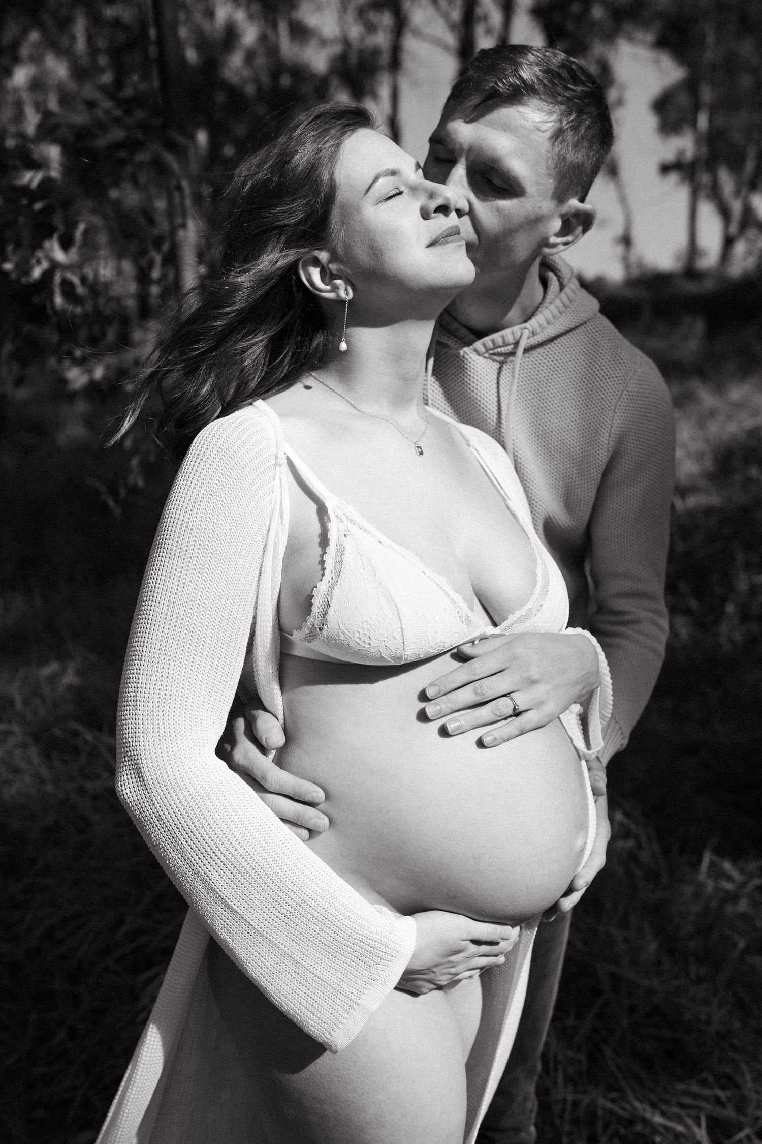 Romantic couple's maternity portrait with white sweater in outdoor setting.